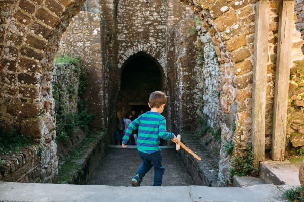 A young child running through archway at Mont Orgueil Castle with a wooden sword
