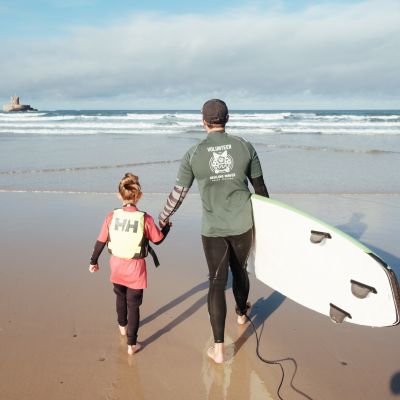 Young girl with surf coach from Healing Waves walking towards the sea in Jersey
