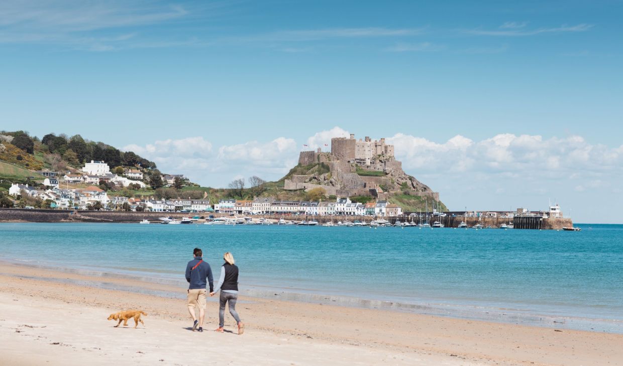 A couple walking their dog on Grouville Beach with Gorey Castle in the background
