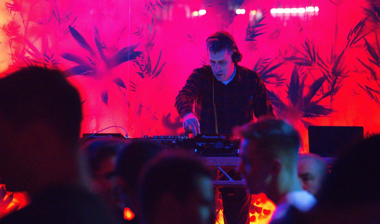 A DJ playing a set with a neon-red background.