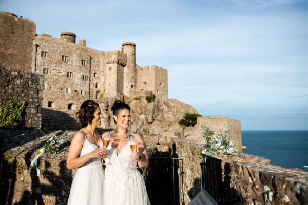 Two brides raising a toast in front of a historic castle
